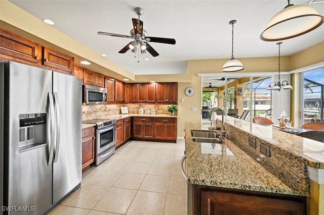 kitchen with light stone countertops, appliances with stainless steel finishes, backsplash, sink, and pendant lighting