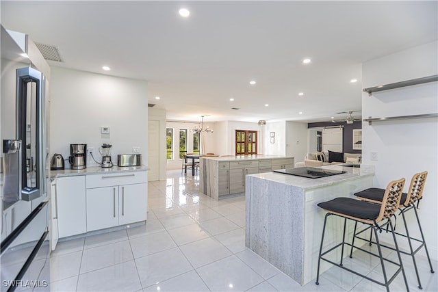 kitchen with white cabinetry, a center island, light stone counters, light tile patterned floors, and ceiling fan with notable chandelier