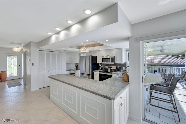 kitchen featuring kitchen peninsula, tasteful backsplash, stainless steel appliances, a tray ceiling, and white cabinets