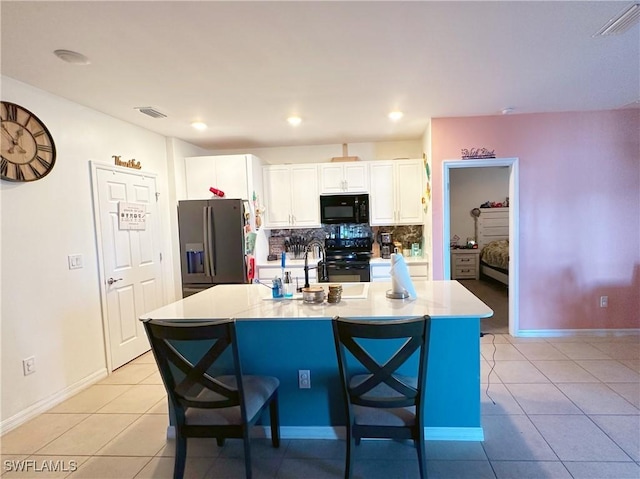 kitchen with an island with sink, white cabinets, a kitchen breakfast bar, and black appliances