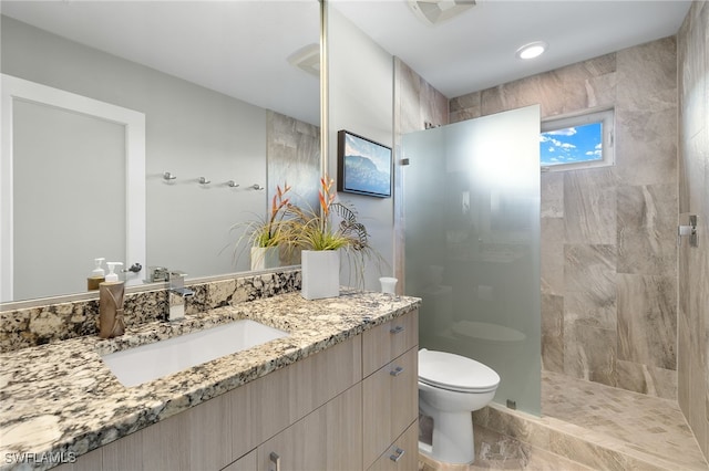 bathroom featuring a tile shower, vanity, and toilet