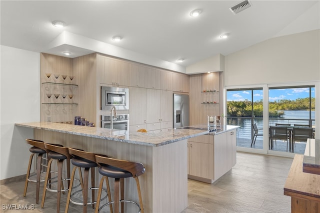 kitchen featuring light stone countertops, light hardwood / wood-style floors, lofted ceiling, a water view, and appliances with stainless steel finishes