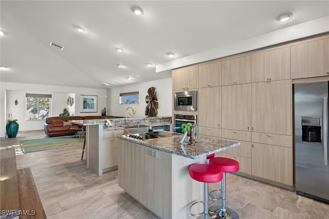 kitchen with a breakfast bar, light stone countertops, a large island with sink, and appliances with stainless steel finishes