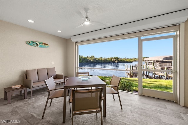 dining space with ceiling fan, a water view, and a textured ceiling