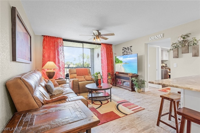 living room featuring ceiling fan, floor to ceiling windows, light wood-type flooring, and a textured ceiling