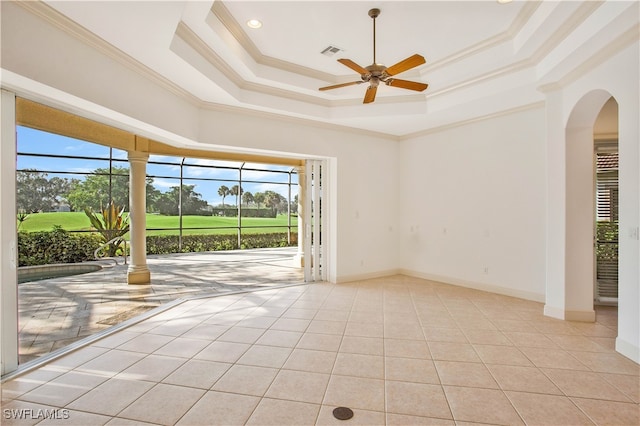 tiled empty room featuring a raised ceiling, a wealth of natural light, ceiling fan, and ornamental molding