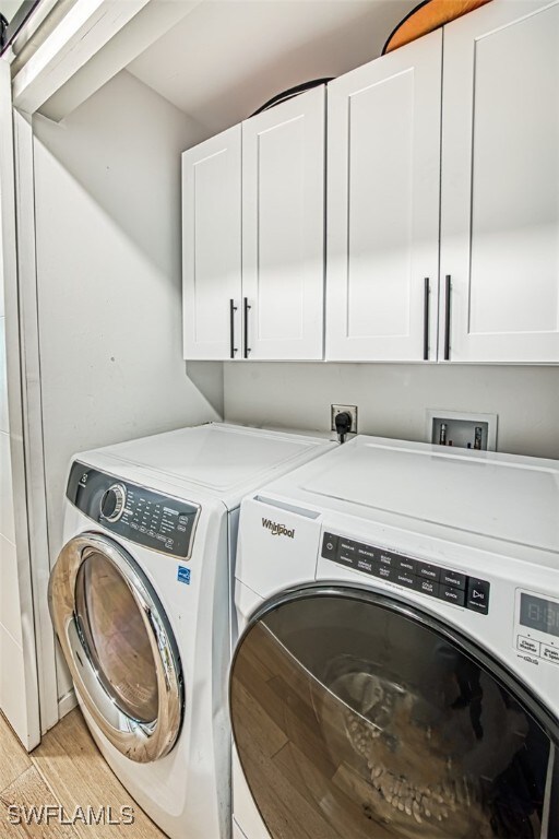 laundry room with cabinets, washer and dryer, and light wood-type flooring