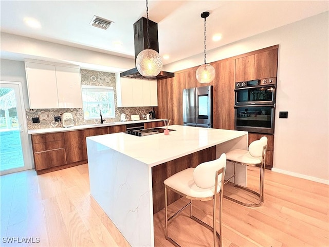 kitchen featuring stainless steel fridge, a kitchen island with sink, hanging light fixtures, white cabinets, and a kitchen bar