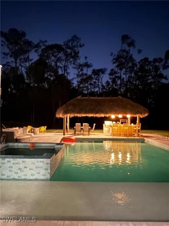 pool at twilight with a hot tub, a gazebo, a patio area, and a bar