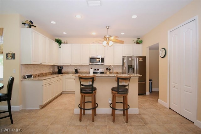 kitchen with light stone countertops, ceiling fan, stainless steel appliances, backsplash, and a center island with sink