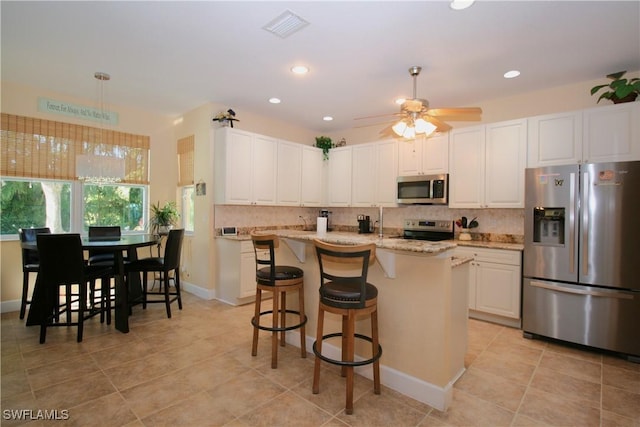 kitchen with light stone countertops, white cabinetry, ceiling fan, stainless steel appliances, and an island with sink