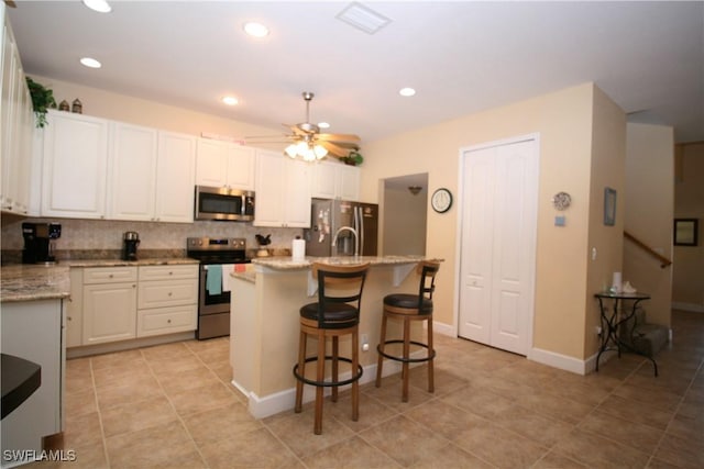 kitchen with light stone countertops, white cabinetry, stainless steel appliances, decorative backsplash, and a kitchen island with sink