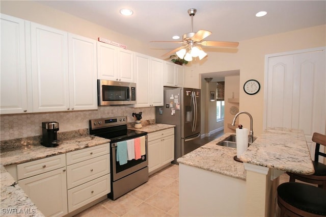 kitchen with sink, light stone counters, a kitchen island with sink, a breakfast bar, and appliances with stainless steel finishes