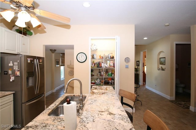 kitchen with stainless steel refrigerator with ice dispenser, light stone counters, ceiling fan, sink, and white cabinets