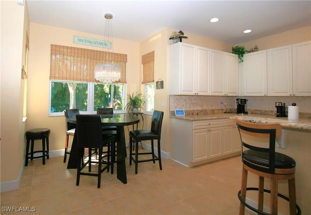 kitchen with white cabinetry, light stone countertops, a kitchen breakfast bar, a chandelier, and pendant lighting