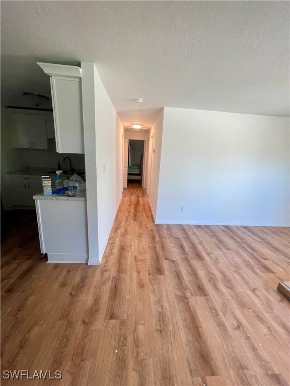 hallway featuring sink, light wood-type flooring, and a textured ceiling