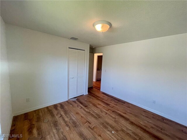 unfurnished bedroom with wood-type flooring, a textured ceiling, and a closet