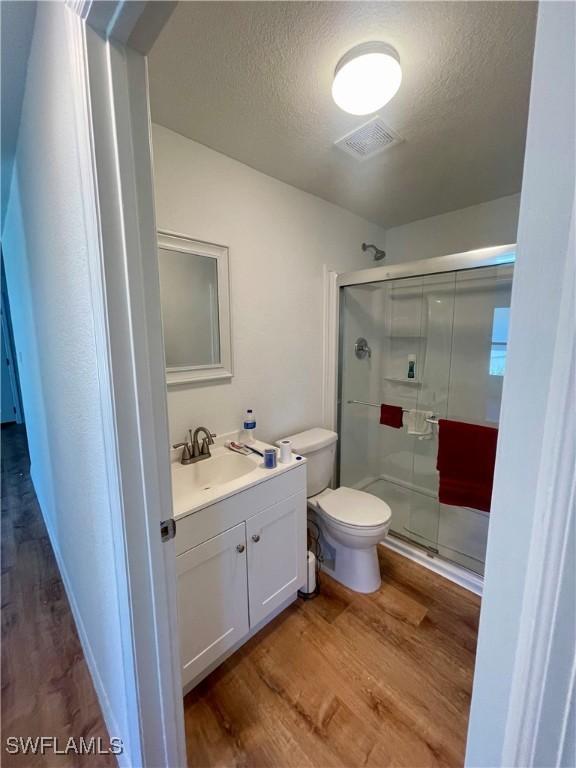 bathroom featuring vanity, a shower with door, toilet, a textured ceiling, and wood-type flooring