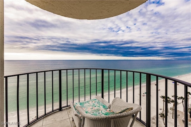 balcony at dusk with a water view and a view of the beach