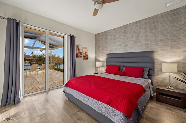 bedroom with an accent wall, wood finished floors, access to outside, and ceiling fan