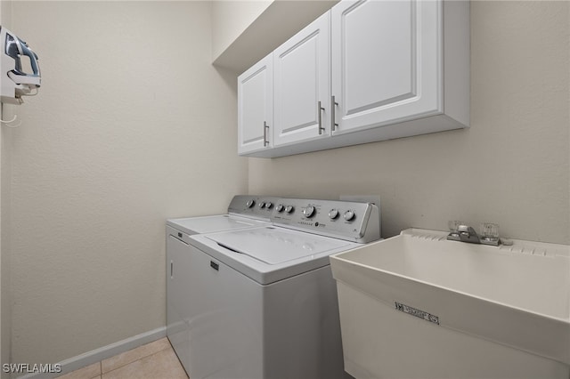 clothes washing area featuring a sink, cabinet space, light tile patterned floors, baseboards, and washer and dryer