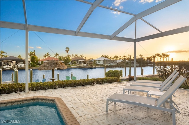 pool at dusk featuring a lanai, a patio area, and a water view