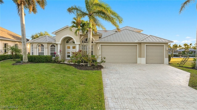 mediterranean / spanish house featuring stucco siding, a standing seam roof, decorative driveway, a front yard, and an attached garage