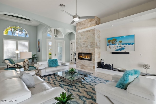 living room featuring ceiling fan with notable chandelier, light tile patterned floors, a high ceiling, and a tiled fireplace