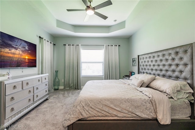 bedroom featuring a raised ceiling, ceiling fan, and light carpet