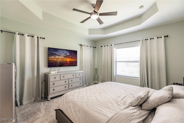 bedroom with light colored carpet, a raised ceiling, and ceiling fan