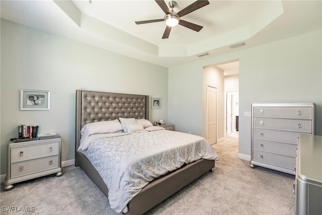 bedroom with ceiling fan, a closet, light carpet, and a tray ceiling