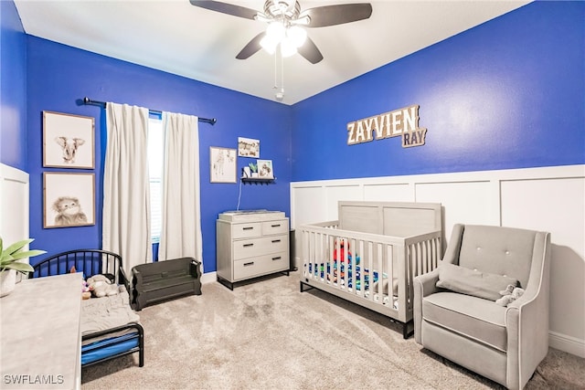 carpeted bedroom with a crib and ceiling fan