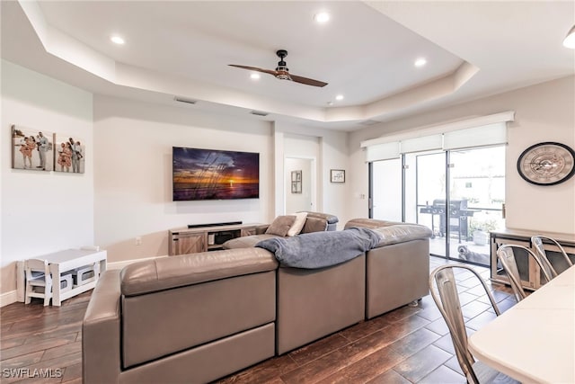 living room featuring a tray ceiling, ceiling fan, and dark wood-type flooring