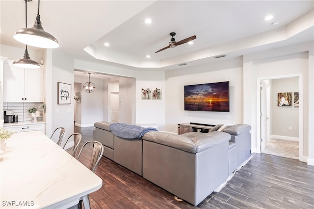 living room featuring ceiling fan, dark hardwood / wood-style flooring, and a tray ceiling