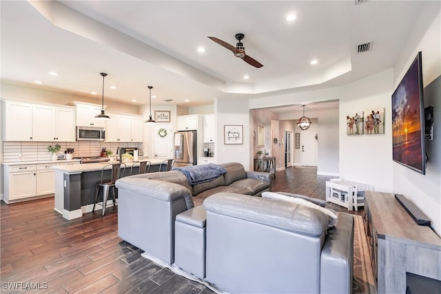 living room with a tray ceiling, ceiling fan, and dark wood-type flooring