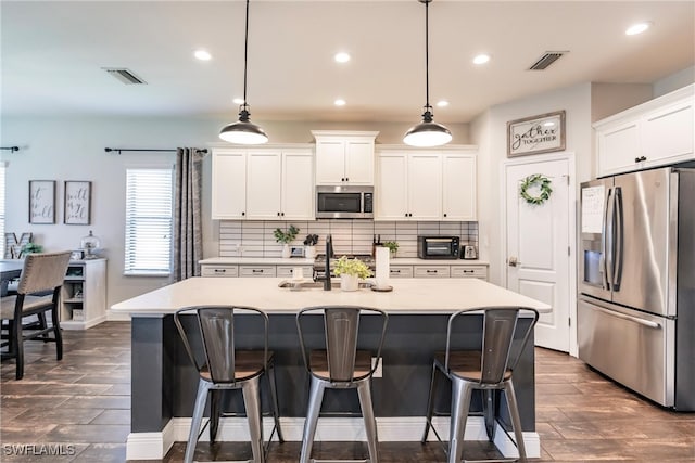 kitchen featuring white cabinets, appliances with stainless steel finishes, decorative light fixtures, and a kitchen island with sink