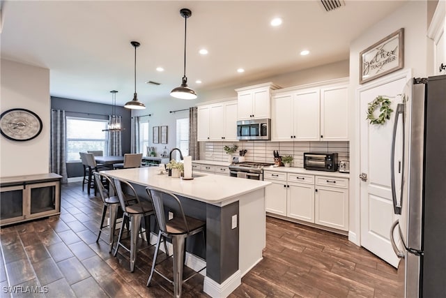 kitchen with white cabinets, decorative light fixtures, an island with sink, and appliances with stainless steel finishes