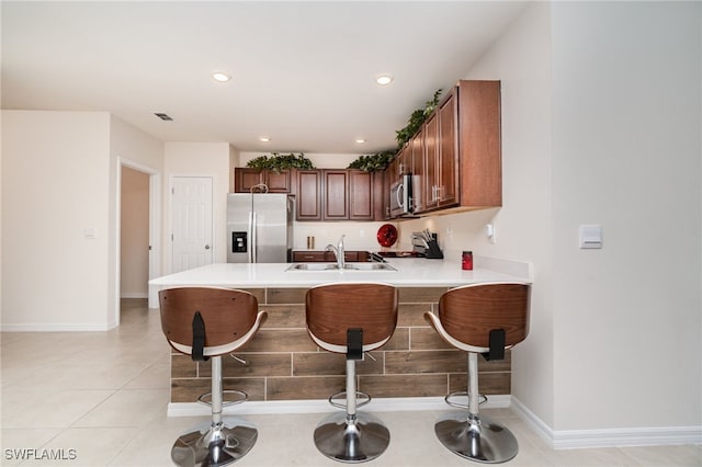 kitchen featuring sink, a kitchen breakfast bar, kitchen peninsula, light tile patterned flooring, and appliances with stainless steel finishes