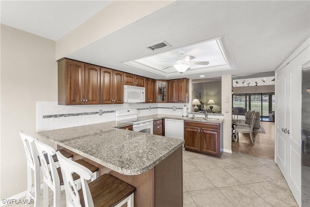 kitchen featuring ceiling fan, a peninsula, white appliances, visible vents, and a raised ceiling