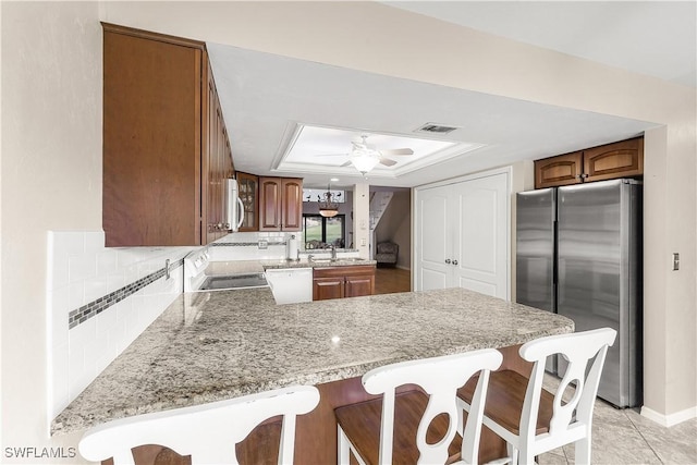 kitchen with a peninsula, white appliances, a ceiling fan, decorative backsplash, and a tray ceiling