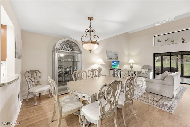 dining area featuring vaulted ceiling, light wood-style flooring, and baseboards