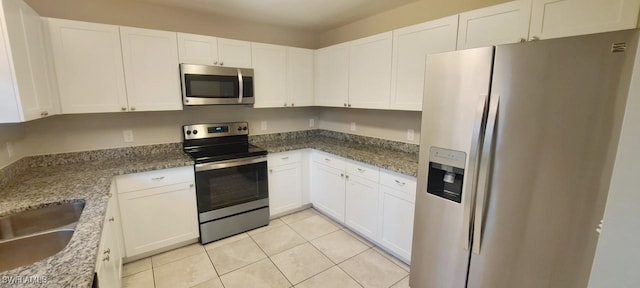 kitchen with appliances with stainless steel finishes, sink, light tile patterned floors, stone countertops, and white cabinetry