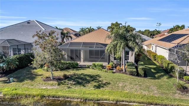 back of property with a water view, a lanai, and a lawn