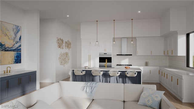 kitchen featuring backsplash, oven, wall chimney range hood, hanging light fixtures, and light hardwood / wood-style flooring