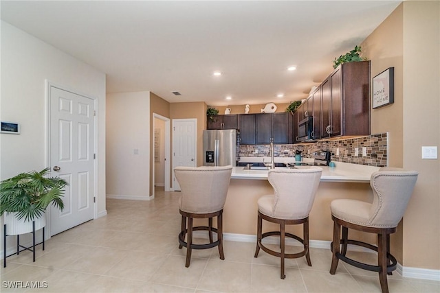 kitchen featuring dark brown cabinetry, a peninsula, stainless steel appliances, light countertops, and backsplash