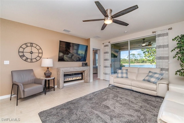 tiled living area featuring a ceiling fan, a glass covered fireplace, visible vents, and baseboards