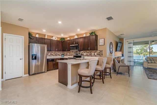 kitchen with a peninsula, visible vents, open floor plan, dark brown cabinets, and appliances with stainless steel finishes