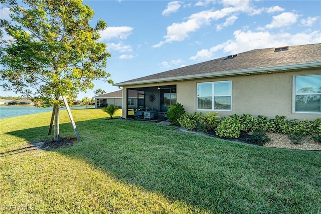 rear view of property with a lawn, a sunroom, roof with shingles, a water view, and stucco siding