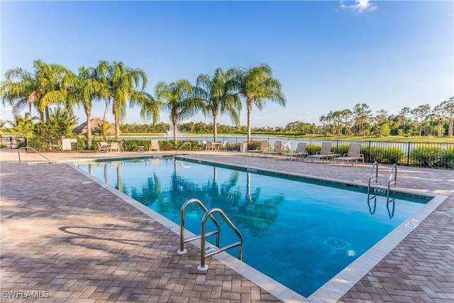 pool with a patio, a water view, and fence