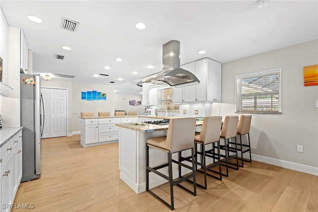 kitchen featuring kitchen peninsula, a kitchen bar, white cabinetry, island exhaust hood, and stainless steel appliances